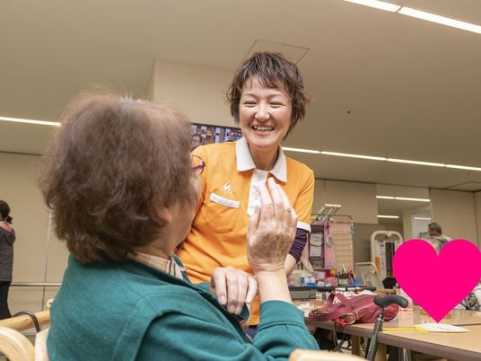 オレンジのポロシャツを着た女性スタッフが眼鏡をかけた女性入居者と話している様子。