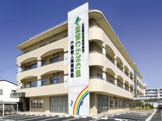 ４階建てのベージュの建物は各フロアにベランダが付き、外壁には虹のイラストとホーム名が書かれている。