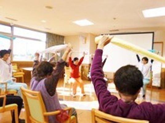 タオルを両手で頭の上で伸ばし、体操をしている入居者とスタッフ。