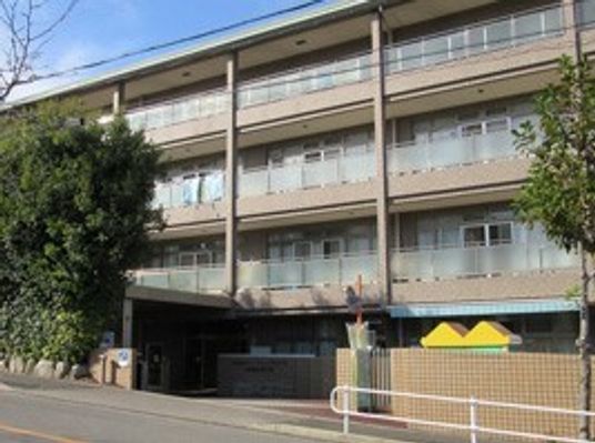 4階建ての建物はベージュ系で各フロアにベランダがあり、敷地内には木が植えられている。