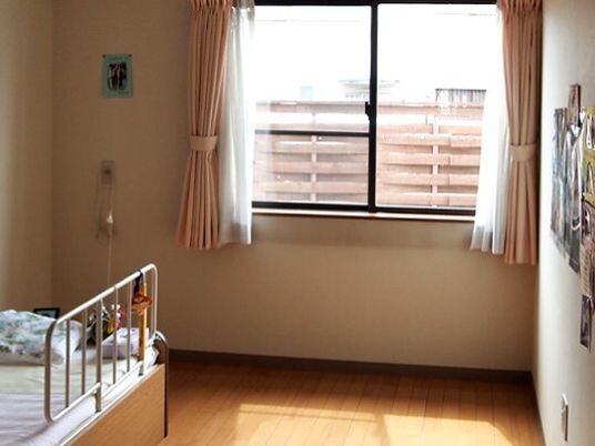 カーテンが付いた窓が設置されたフローリングの居室には寝具付きのベッドが置かれ、写真が貼られている。