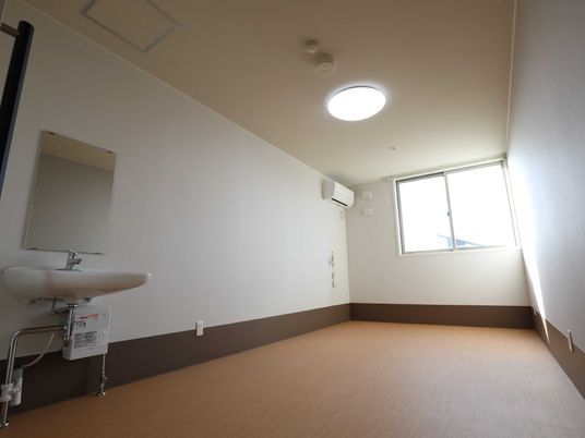 エアコンと車いす対応の洗面所が付いたシンプルな部屋。壁には緊急通報装置が付いている。