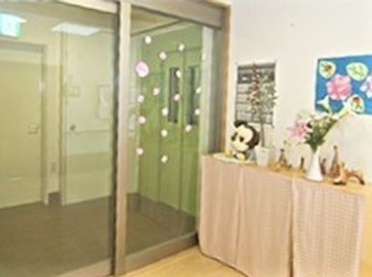 自動ドアの玄関の横には棚があり、ぬいぐるみや花、作品などが飾られている。