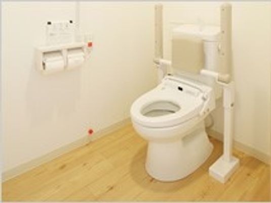 トイレの両サイドに可動式の手すりが付き、背もたれもある。介助用のスペースがとても広い。