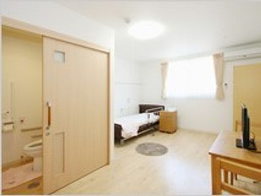 フローリングの広い部屋には収納家具やトイレが付き、窓が大きい。