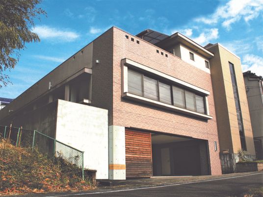 レンガ調の外壁が明るい雰囲気の３階建ての建物。周辺には緑が多くある。