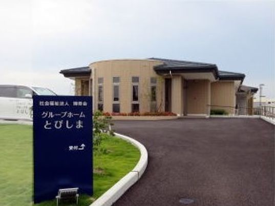 ブラウンを基調とした建物。手前にはグループホームの名前が書かれた黒い石がある。