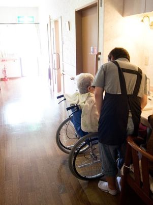 車いすに乗った女性入居者のそばには女性スタッフ。洗面所でサポートしている様子。