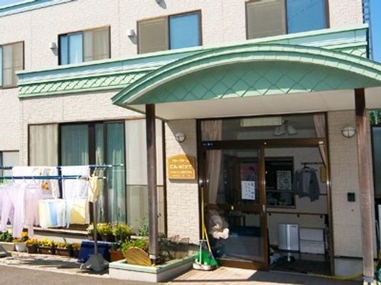 緑の屋根が付いた２階建ての建物。洗濯物干し場や花壇が周りにある。