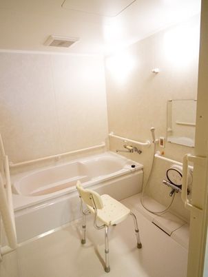 真っ白な浴室には一人用の浴槽や手すり、シャワーチェアやシャワーが設置されている。