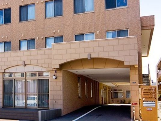 ブラウン調の３階建ての大きな建物。１階部分の玄関付近はくりぬかれ、車で玄関先まで行けるようになっている。
