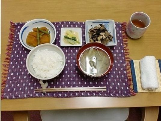 白いご飯に味噌汁、かぼちゃの煮物やあえ物などがランチョンマットに並び、お茶とお絞りが添えられている。