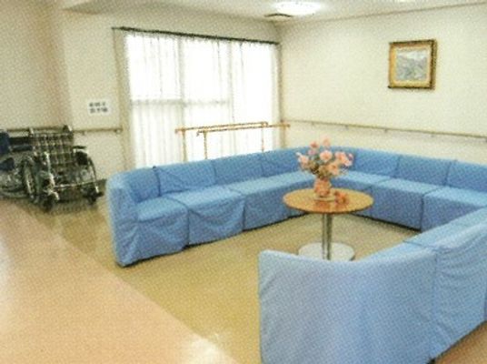 ブルーの大きなソファの後ろには平行棒や車いすが置かれている。