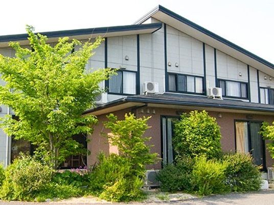 緑に囲まれた2階建ての建物は2階部分が白、1階部分がブラウン。