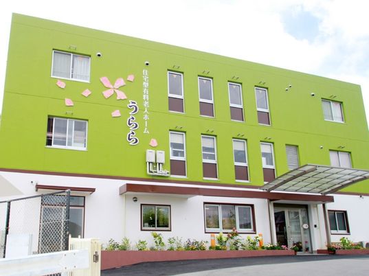 3階建ての建物は1階部分が白、2階より上は黄緑で、ホーム名と桜の絵が外壁に書かれている。