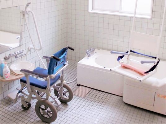 白い浴槽が設置された浴室。シャワーや手すり、浴室用の車いすやリフトも設置されている。