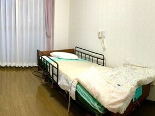 ベッドサイドには緊急通報装置があり、ベッドには寝具が設置され、窓にはカーテンがある。