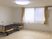 エアコンが付いたフローリングの部屋にはマットレスがない介護ベッドが置かれ、レースカーテンとカーテンが付いた大きな窓がある。