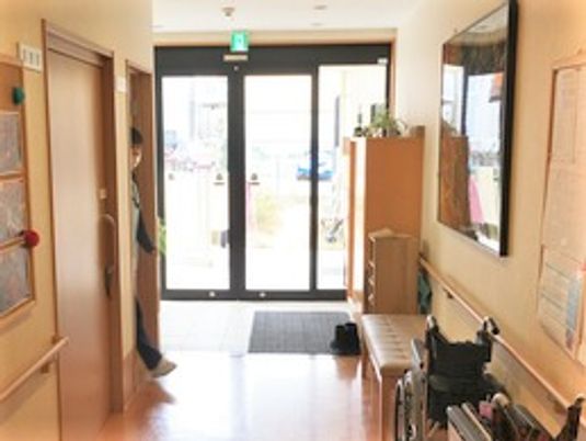 施設のエントランス部分を写した写真。両側に手すり付きの廊下、個室の入り口が写っている