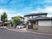 グレーの屋根が付いた２階建ての建物は敷地内には駐車場があり、車が止まっている。