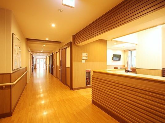 手前にスタッフステーションがある施設内の共有スペースの様子。手すりがついているオールバリアフリーの廊下