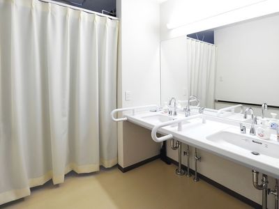 車いす対応の洗面所が二つ並び、大きな鏡が付いている。右手にはカーテンが付けられている。