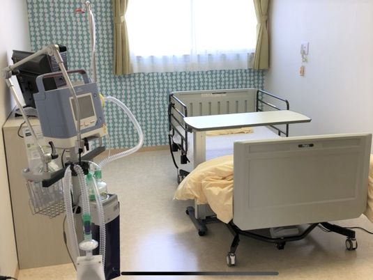 緑あふれる環境の中、屋外での散歩を楽しむ眼鏡の高齢男性とエプロン姿の女性。