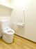 エル字型の手すりやオレンジの呼び出しボタンが付いたトイレは広く、ふたのない便座が設置されている。
