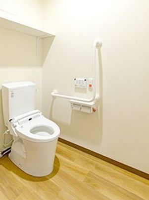 エル字型の手すりやオレンジの呼び出しボタンが付いたトイレは広く、ふたのない便座が設置されている。
