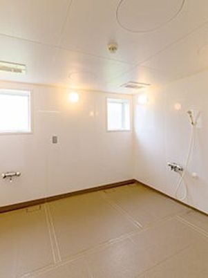 浴槽や機械浴は置かれておらず、シャワーのみ壁についている。窓や照明があり、明るい浴室。