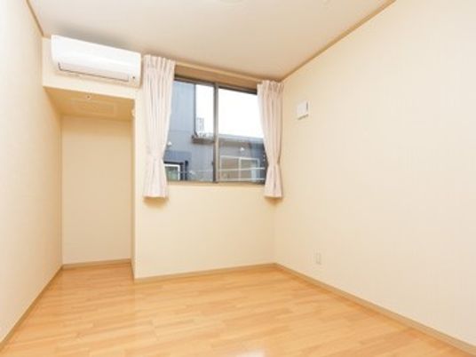 フローリングの居室。大きな窓とエアコンが付いたシンプルな洋風の部屋。