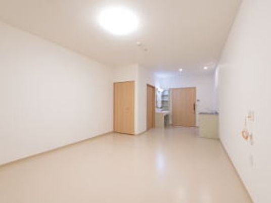 二人用の広い居室には家具が置かれておらず、壁には緊急通報装置が設置され、奥にはクローゼットや洗面所、キッチンがある。