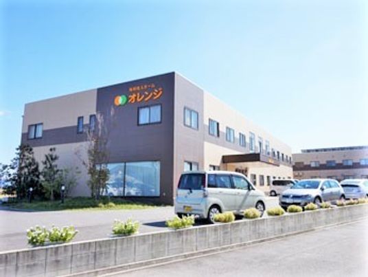 2階建ての建物はベージュ系の外観で、屋外に広い駐車場を設置している。