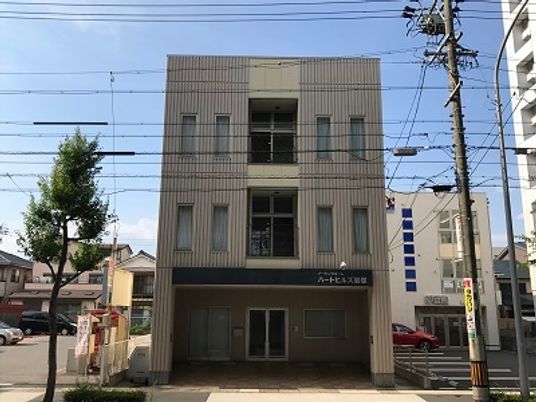 3階建ての建物の玄関には屋根があり、施設名が書かれている。周辺には駐車場がたくさん設置されている。