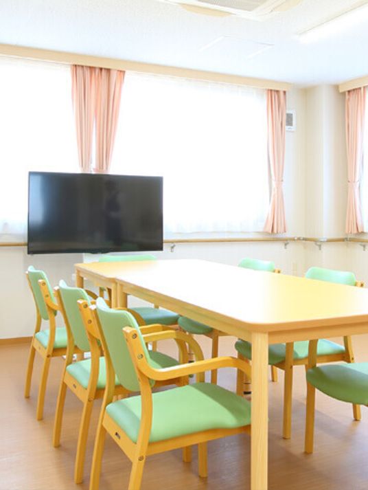 テレビが置いてある施設内のリビングスペースの様子。テーブルと椅子が並べられている写真
