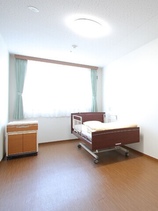 タンスと介護用ベッドが置かれている入居前の部屋。施設の居室の写真