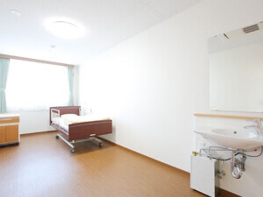洗面台と介護用ベッドなどがついた施設の居室の様子。オールバリアフリーの床が写っている様子