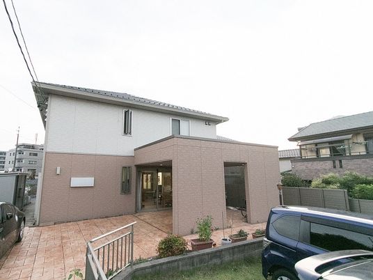 2階建ての建物。ブラウンと白のモダンなデザインで建物周辺のプランターには花も植えられている。