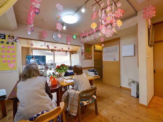 ピンクの花が天井からたくさんぶら下がっているリビングダイニングでは女性たちがテレビを見ている。