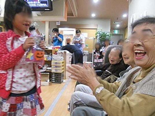 赤いジャケットを着た女の子が入居者にハロウィンのプレゼントをあげようとしているところ。満面の笑顔の入居者。