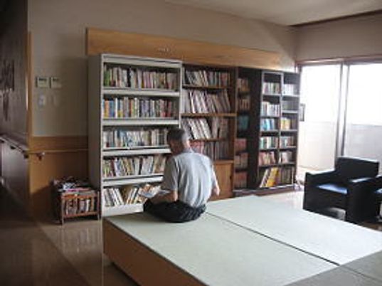 大きな本棚が並べられ、所狭しと本が収められている。畳の小上がりスペースやソファが置かれ、男性が読書をしている。