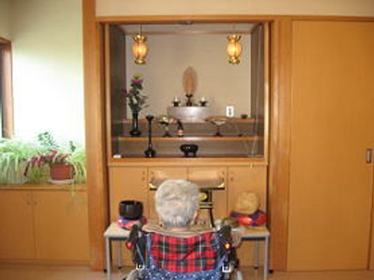 家具調の仏壇の前には木魚などが置かれ、入居者がお参りをすることができる。車いすの入居者が仏壇の前にいる。