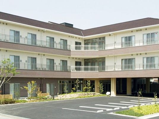 エル字型の３階建ての建物の各フロアにベランダがあり、敷地内には草木が植えられ、駐車場も付いている。