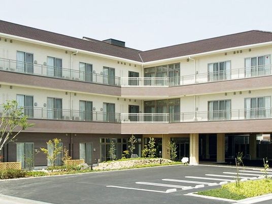 エル字型の３階建ての建物の各フロアにベランダがあり、敷地内には草木が植えられ、駐車場も付いている。
