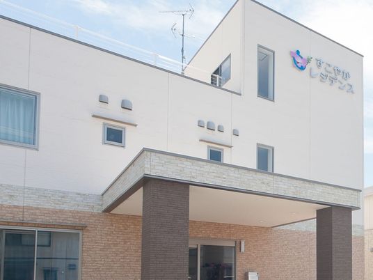 ベージュの2階建ての建物。外壁にはホーム名が書かれ、玄関には車寄せが付いている。