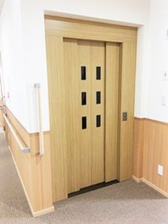 木製のエレベーターのドアの様子。左側に手すり付きの階段がある