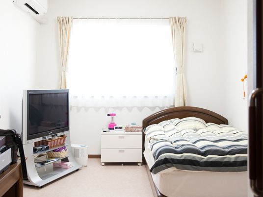 部屋の中にテレビと介護用ベッド、エアコンが並んでいる様子。物入の引き出しが置いてある