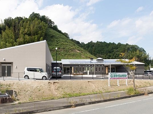 広い駐車場が付いたブラウン系の建物。玄関には車寄せがあり、玄関前には緩やかなスロープが付いている。