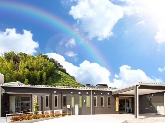 ブラウン系の平屋建ての建物には二つ玄関があり、上空には虹が出ている。