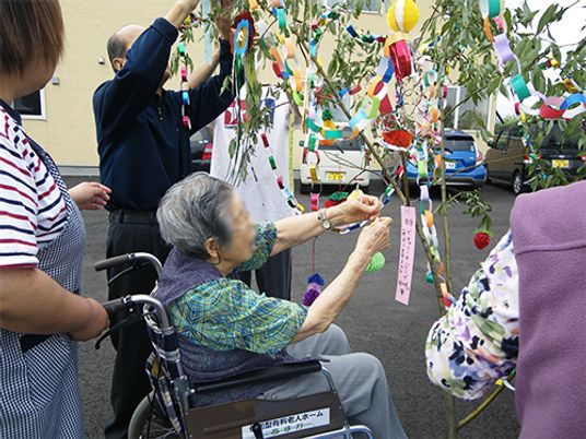 七夕飾りを付けている車いすの女性入居者。そばにはスタッフがいる。